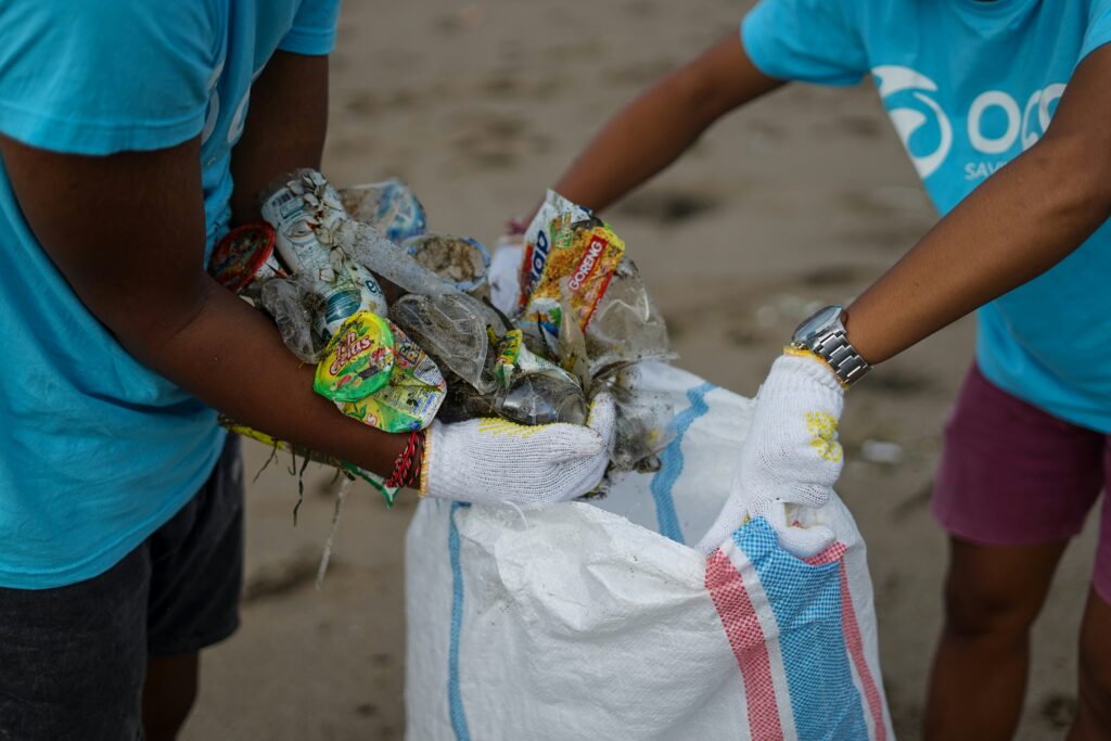Twee mensen gooien plastic afval in een vuilniszak tijdens een beach clean up